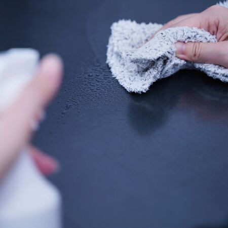 Young woman is holding spray bottle, rag to clean, wipe down office metal cabinet shelf...