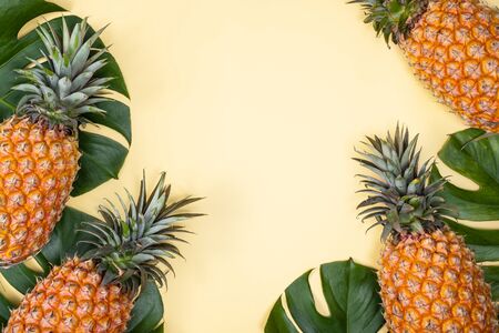 Beautiful pineapple on tropical palm monstera leaves isolated on bright pastel yellow background,...