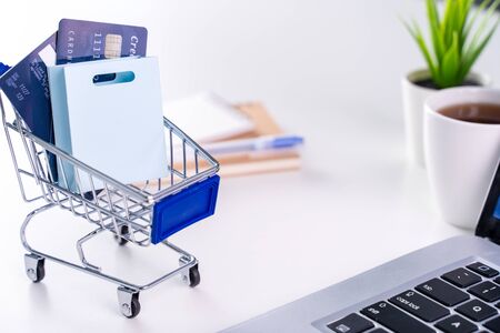 Office online paying, stay home shopping, electronic payment with credit card concept, laptop on white table background with shop cart, close up.の写真素材