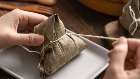 Dragon Boat Festival food - Rice dumpling zongzi, young Asian woman eating Chinese traditional food on wooden table at home celebration, close upの写真素材