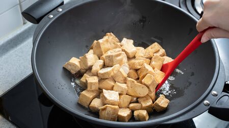 Cooking diced cubed dried tofu on gas stove in home kitchen, lifestyle, closeup.の写真素材