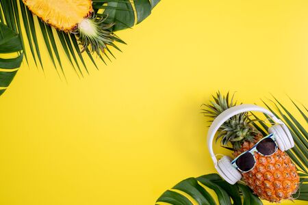 Funny pineapple wearing white headphone, listen music, isolated on yellow background with tropical palm leaves, top view, flat lay design concept.の写真素材