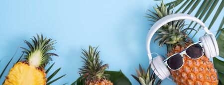 Funny pineapple wearing white headphone, concept of listening music, isolated on colored background with tropical palm leaves, top view, flat lay design.の写真素材