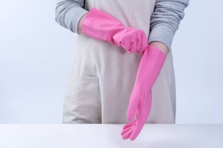 Young woman housekeeper in apron is wearing pink gloves to clean the table, concept of preventing virus infection, housekeeping service, close up.の写真素材