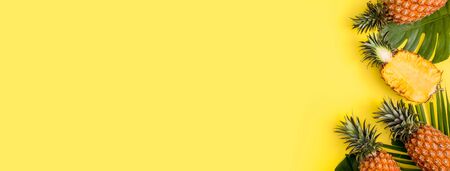 Beautiful pineapple on tropical palm monstera leaves isolated on bright pastel yellow background, top view, flat lay, overhead above summer fruit.の写真素材