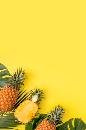 Beautiful pineapple on tropical palm monstera leaves isolated on bright pastel yellow background,...