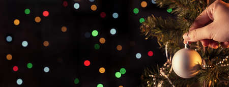 Christmas background concept- beautiful decor bauble hanging on the Christmas tree with sparkling light spot, blurry dark black background, copy space, close up.の写真素材