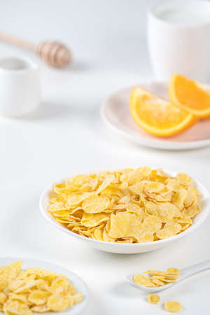 Corn flakes bowl sweeties with milk and orange on white background, close up, fresh and healthy...