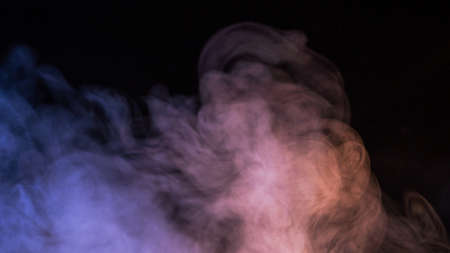 Conceptual image of multi-colored smoke isolated on dark black background and wooden table.の写真素材