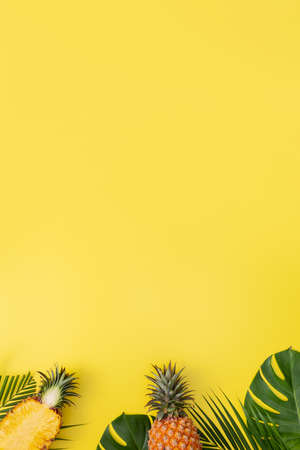 Beautiful pineapple on tropical palm monstera leaves isolated on bright pastel yellow background, top view, flat lay, overhead above summer fruit.の写真素材