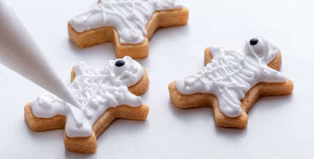 Close up of decorating cute Halloween gingerbread cookies with frosting icing cream topping bag.の写真素材