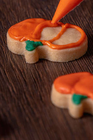 Close up of decorating cute Halloween pumpkin gingerbread cookies with frosting icing cream topping bag.の写真素材