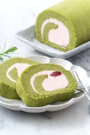 Delicious Matcha Swiss Roll Cake slices with strawberry icing cream on white background, close up.の写真素材