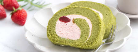 Delicious Matcha Swiss Roll Cake slices with strawberry icing cream on white background, close up.の写真素材