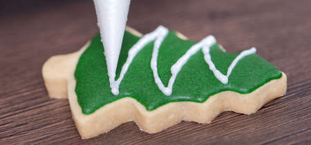 Close up of drawing gingerbread Christmas tree sugar cookie on wooden table background with green...