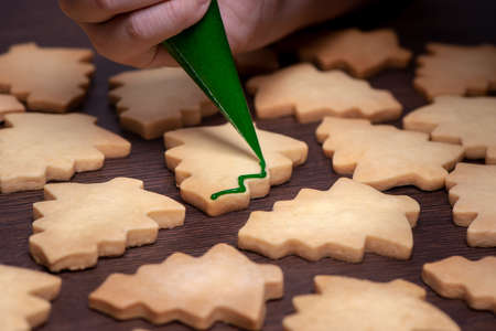 Close up of drawing gingerbread Christmas tree sugar cookie on wooden table background with green...
