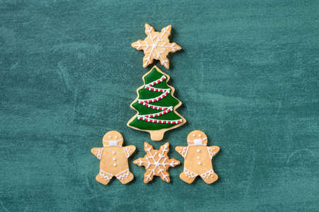 Top view of Christmas tree and snowflake cooikes with gingerbread man wearing mask on green table background.の写真素材
