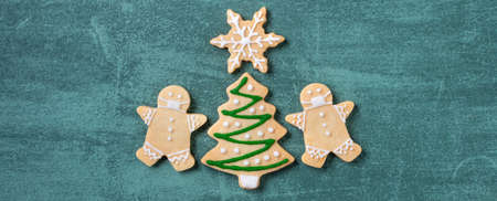 Top view of Christmas tree and snowflake cooikes with gingerbread man wearing mask on green table background.の写真素材