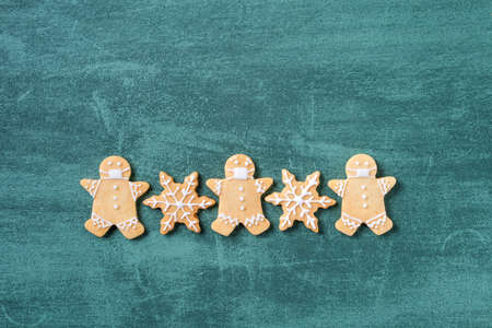 Top view of Christmas tree and snowflake cooikes with gingerbread man wearing mask on green table background.の写真素材