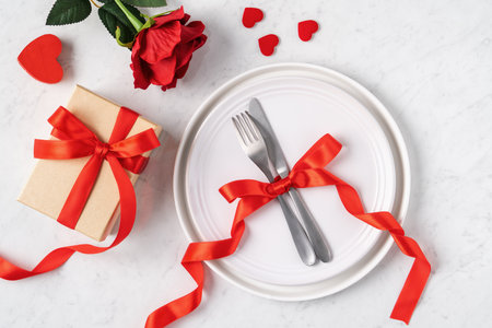 Empty white plate with tableware, ribbon, gift and roses for Valentine's Day special holiday dating meal concept.の写真素材