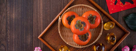 Top view of fresh sweet persimmons kaki with leaves on wooden table background for Chinese lunar new year fruit design concept, the word means blessing is coming.の写真素材