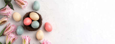 Colorful Easter eggs in the nest with pink lily flower on bright marble white table background.の写真素材