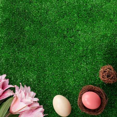 Colorful Easter eggs in the nest with pink lily flower on on a lawn grass background.