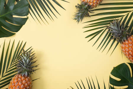 Top view of fresh pineapple with tropical palm and monstera leaves on yellow table background.の写真素材