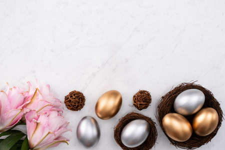Golden and silver Easter eggs in the nest with pink lily flower on bright marble white table background.の写真素材