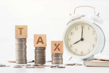 Concept of tax season approaching with wooden blocks, coins and alarm clock over white background.の写真素材