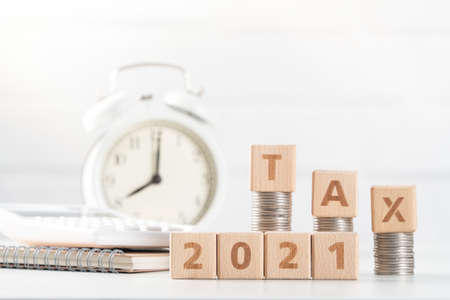 Concept of tax season approaching with wooden blocks, coins and alarm clock over white background.の写真素材