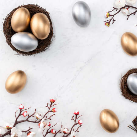 Design concept of Golden and silver Easter eggs in the nest with white plum flower on bright marble white table background.の写真素材