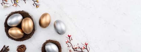 Design concept of Golden and silver Easter eggs in the nest with white plum flower on bright marble white table background.の写真素材