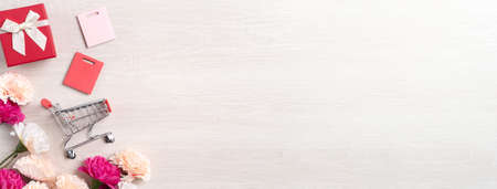 Design concept of Mother's Day greeting with carnation flower, holiday gift idea and shopping cart on wooden background.の写真素材