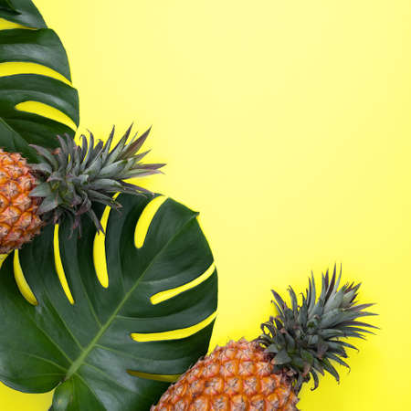 Top view of fresh pineapple with tropical palm and monstera leaves on yellow table background.の写真素材