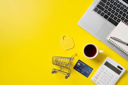 Top view of online shopping design concept with credit card, note, calculator and computer isolated on office yellow table background.の写真素材
