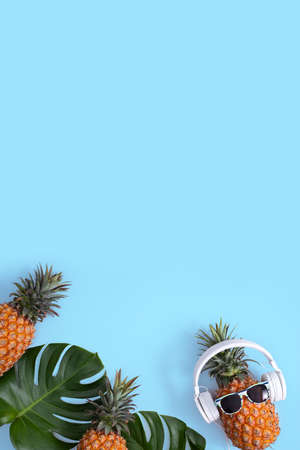Funny pineapple wearing white headphone, concept of listening music, isolated on blue background with tropical palm leaves, top view, flat lay design.の写真素材