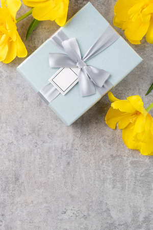 Mother's day background concept. Top view design of holiday greeting gift with yellow tulip bouquet on bright gray table backgroundの写真素材