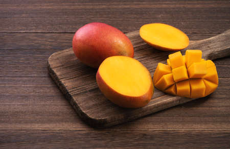 Mango. Close up of fresh ripe mango fruit with leaves over dark wooden table background with green...