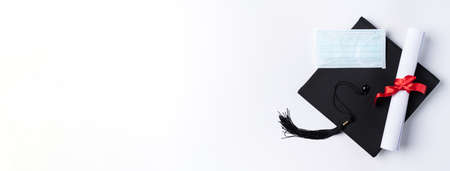 Top view of graduation square academic cap with degree diploma and mask isolated on white table background.の写真素材