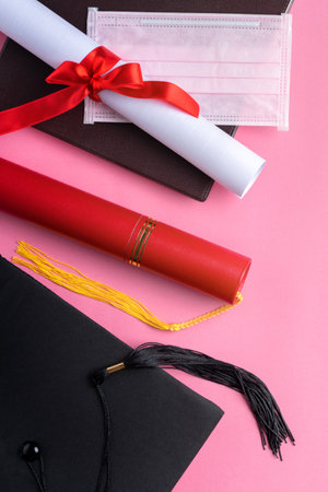 Top view of graduation square academic cap with degree diploma and mask isolated on pink table background.の写真素材
