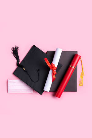 Top view of graduation square academic cap with degree diploma and mask isolated on pink table background.の写真素材