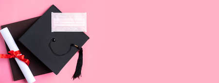 Top view of graduation square academic cap with degree diploma and mask isolated on pink table background.の写真素材