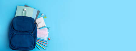 Top view of blue backpack with school stationery over blue table background, back to school design...