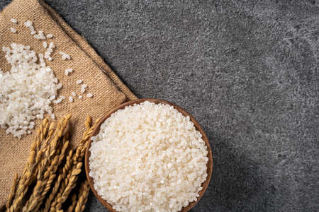 White raw rice in a bowl with the ear on the dark black table background.の写真素材