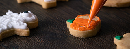 Close up of decorating cute Halloween pumpkin gingerbread cookies with frosting icing cream topping bag.の写真素材
