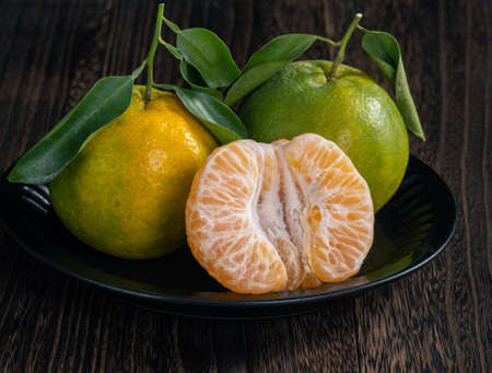Fresh green tangerine mandarin orange with fresh leaves on dark wooden table with black background harvest concept.の写真素材