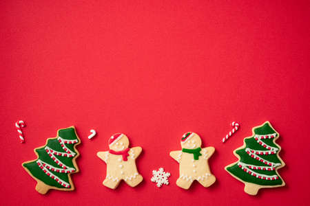 Top view of decorated Christmas gingerbread cookies with decorations on red table background with...