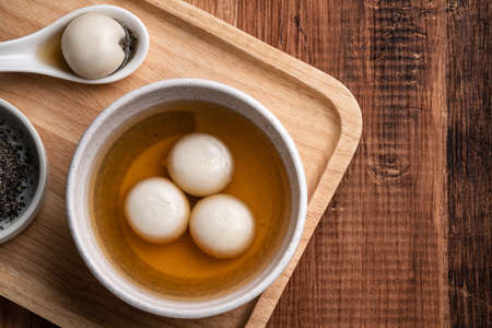Top view of sesame big tangyuan (tang yuan, glutinous rice dumpling balls) with sweet syrup soup in a bowl on wooden table background for Winter solstice festival food.の写真素材