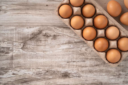 Top view of fresh brown chicken eggs in a kraft paper egg carton on wooden table background.